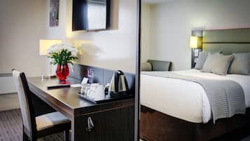 A hotel room with a bed, a desk with a vase of flowers, a television, and a lamp.