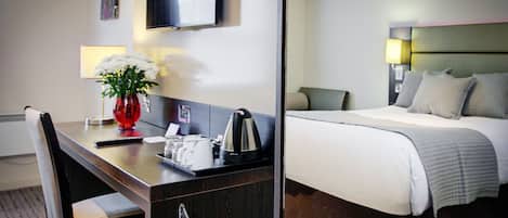 Habitación de hotel con cama, escritorio con un florero, televisión y lámpara.