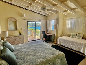 A hotel room with a bed, a desk, a chair, a dresser, a ceiling fan, and a view of the ocean. - Spectacular beachfront villa. Great SNORKELING, kayaking, sunrise & sunset views (St John)