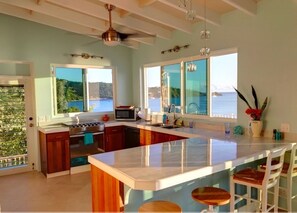 Una cocina moderna con una isla grande, taburetes de bar y vista al mar.