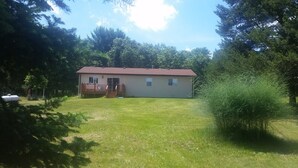 A single-story house with a front porch and a small deck. - SECLUDED WOODLAND ESCAPE NEAR WISCONSIN DELLS WITH POND ON 80 PRIVATE ACRES (Lyndon Station)