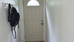A hallway with a white door, a black and white rug, and a coat rack with a backpack. - SECLUDED WOODLAND ESCAPE NEAR WISCONSIN DELLS WITH POND ON 80 PRIVATE ACRES (Lyndon Station)