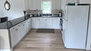A spacious kitchen with white cabinets, a central island, a refrigerator, and a window with a view. - SECLUDED WOODLAND ESCAPE NEAR WISCONSIN DELLS WITH POND ON 80 PRIVATE ACRES (Lyndon Station)
