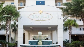 The Pearl hotel entrance with a central fountain, palm trees, and a tiled pathway.