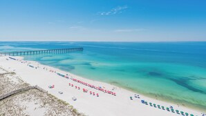 A beach with a pier extending into the water, clear turquoise water, and a row of beach umbrellas.