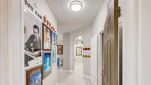 Un couloir avec des tableaux encadrés accrochés aux murs, une porte blanche sur la droite et un luminaire au plafond.