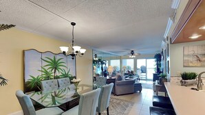 A spacious living area with a dining table, chairs, and a large painting of tropical plants. - Fort Walton Beach Condo with Beachfront Balcony, Views of The Gulf of Mexico, an (Fort Walton Beach)