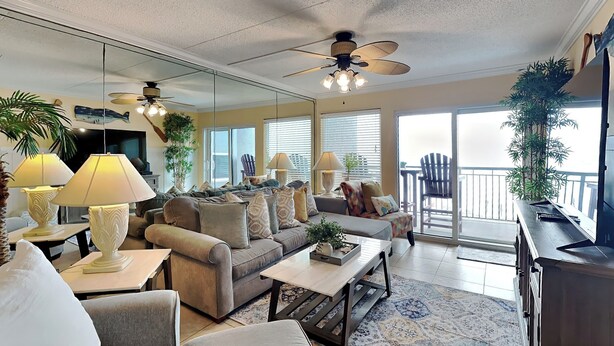 A spacious living room with a gray sofa, two armchairs, a coffee table, and a ceiling fan. There are potted plants and a large mirror on the wall. - Fort Walton Beach Condo with Beachfront Balcony, Views of The Gulf of Mexico, an (Fort Walton Beach)