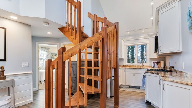 A spacious kitchen with white cabinetry, a wooden staircase, and a large window providing natural light. - Newly updated 3bdrm Dennis Port home 1.5 blocks to the beach! (Dennis)