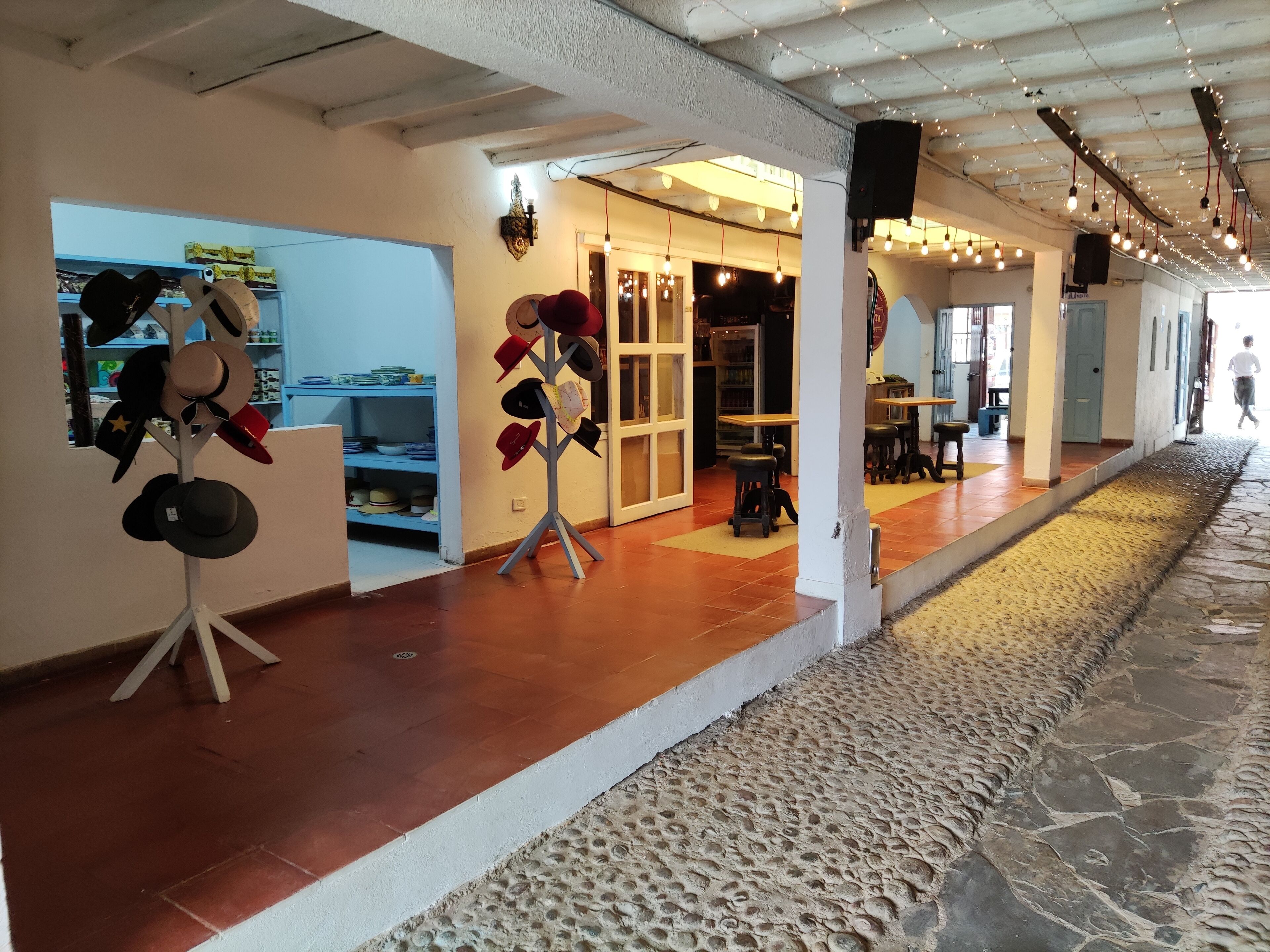 A corridor with a hat rack, shelves with hats, and a doorway leading to a bar area.