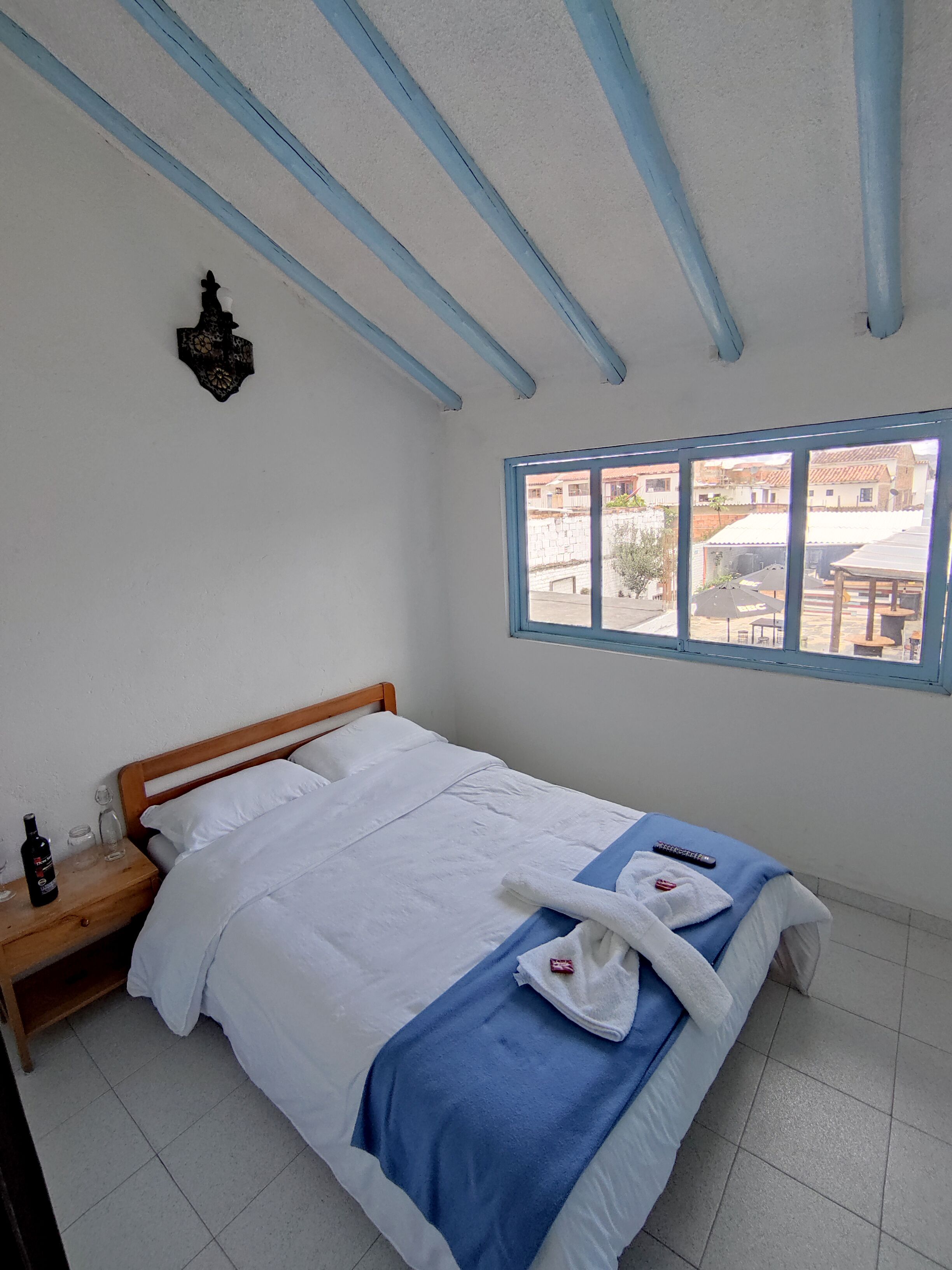 A bedroom with a bed, a nightstand, a window with a view of buildings, and a decorative wall piece.