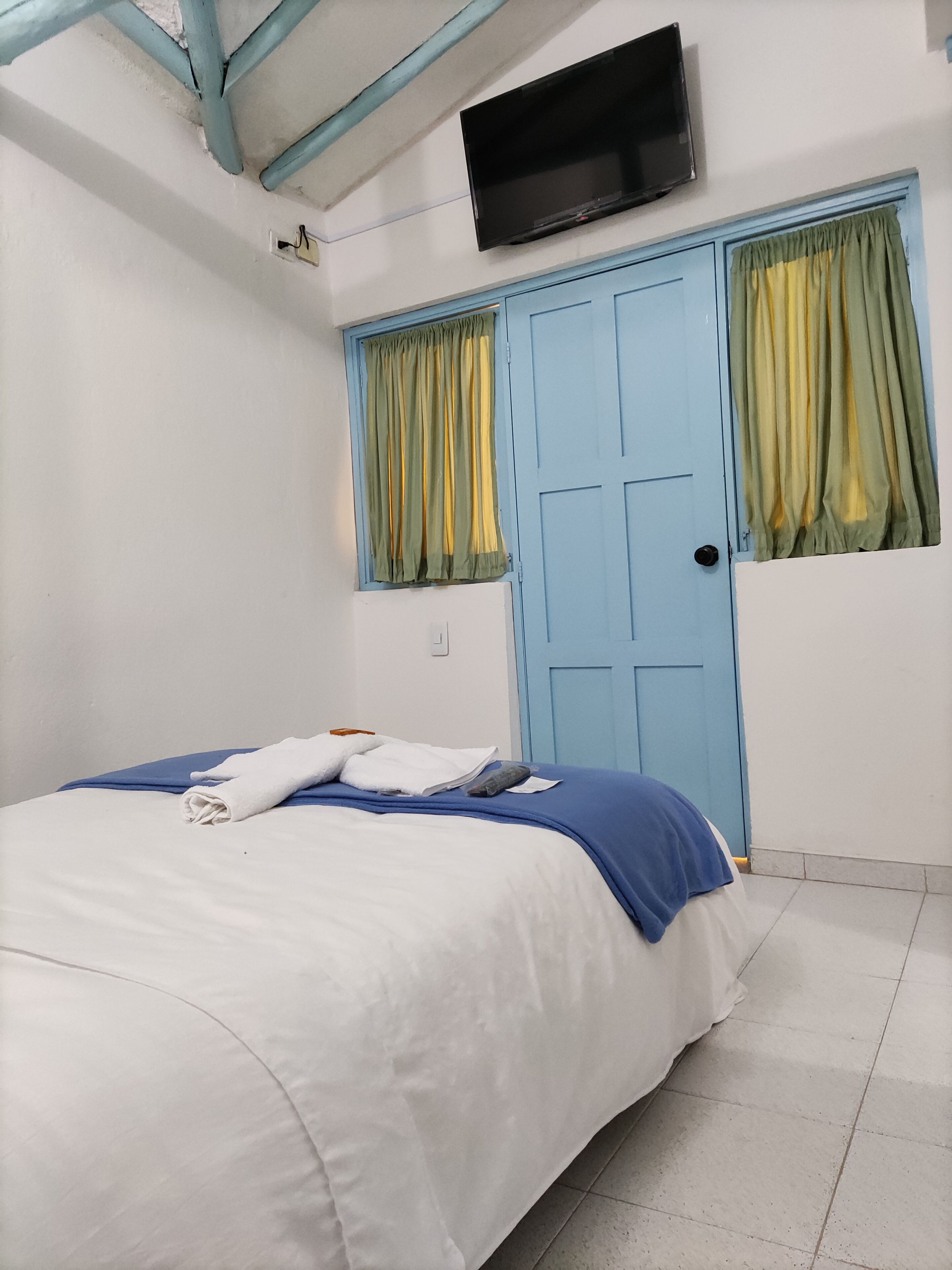 Een slaapkamer met een bed, een aan de muur bevestigde televisie en een deur met gordijnen.