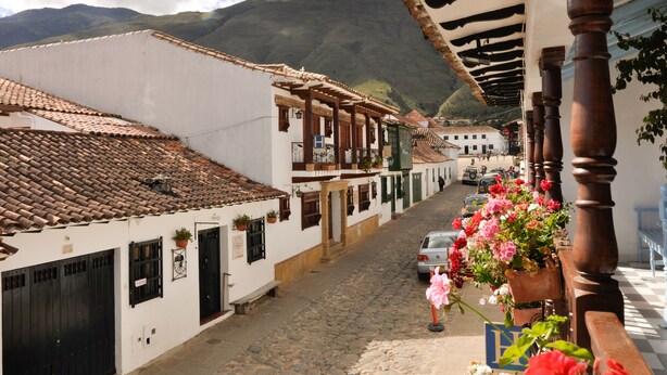 Rua de paralelepípedos flanqueada por edifícios brancos tradicionais, com telhados de azulejos e varandas de madeira.