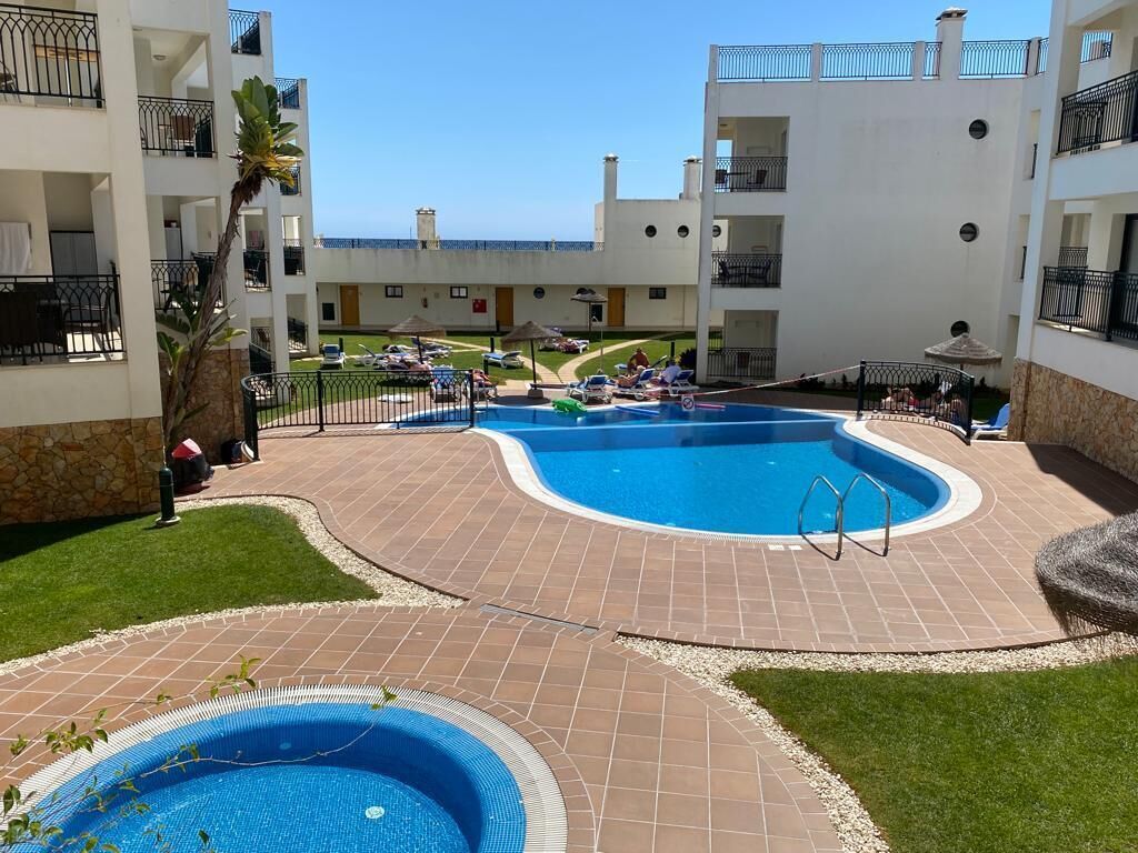 Un espace piscine au design incurvé, entouré d’une terrasse carrelée et d’une petite zone herbeuse.