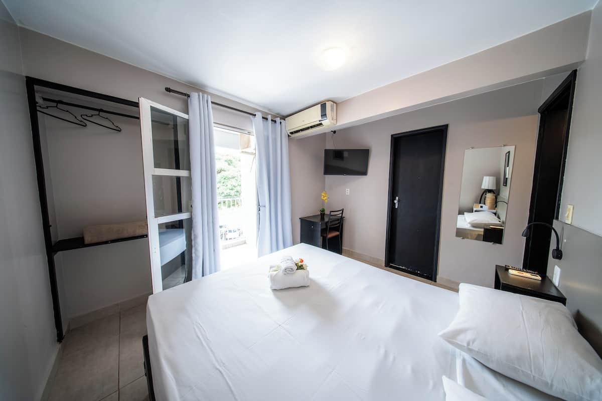 Ein Hotelzimmer mit Bett, Schreibtisch, Stuhl, Kleiderschrank, Spiegel und Klimaanlage.