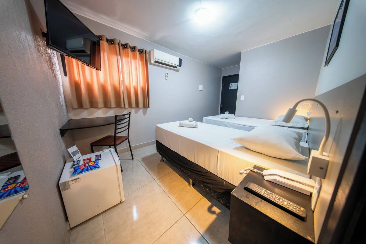 Ein Hotelzimmer mit Bett, Schreibtisch, Stuhl, Fernseher, Klimaanlage und Nachttischlampe.