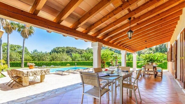 Un patio techado al aire libre con piscina, mesas y sillas de piedra.