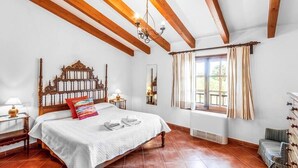 Un dormitorio con cama de madera, lámpara de araña, ventana con cortinas y radiador.