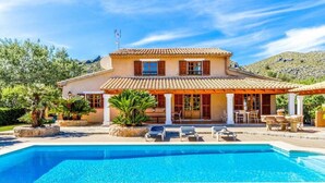 Una casa de dos pisos con piscina, mobiliario de exterior y montañas al fondo.