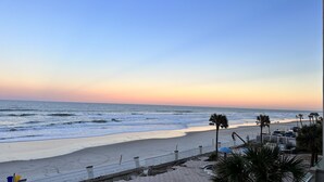 A beach with a paved walkway, palm trees, and a fence along the shore.