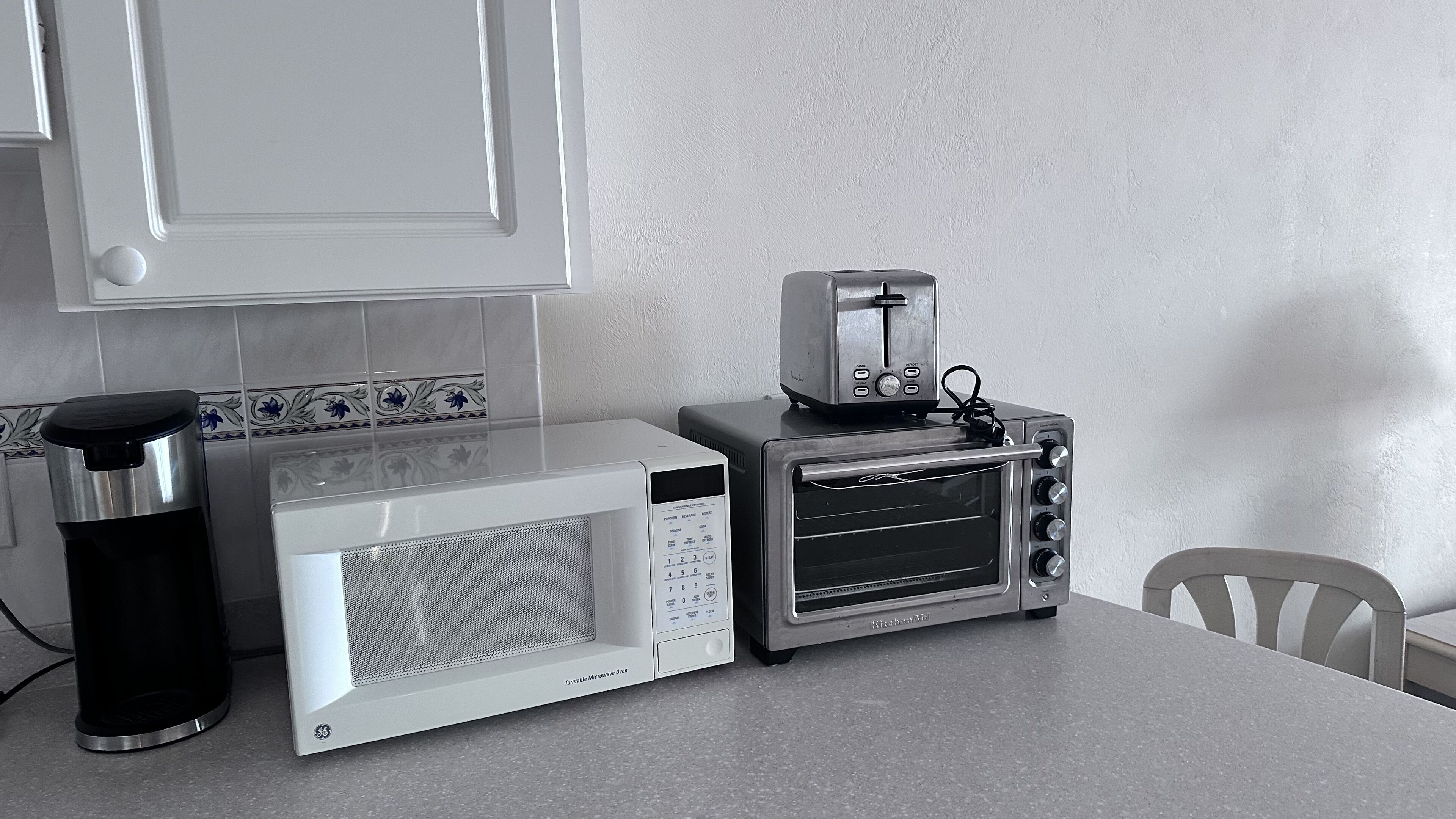 Una cocina con microondas, tostadora y cafetera sobre una encimera.