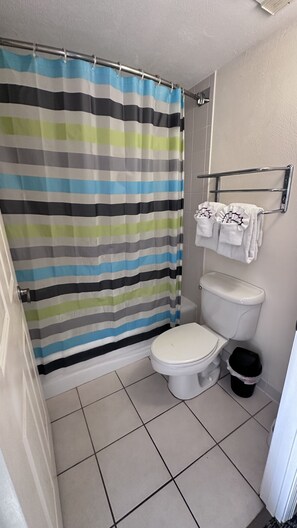 A bathroom with a striped shower curtain, a toilet, a trash bin, and a towel rack with towels. - Josh’s Daytona Beach Resort 1BR Oceanfront Condo 🏖 (Daytona Beach)