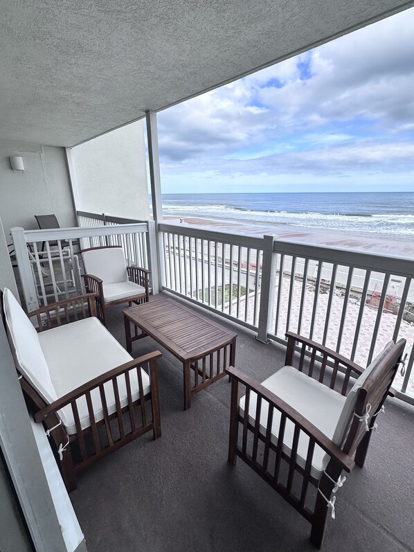 A balcony with a view of the beach, wooden furniture, and a railing. - Josh’s Daytona Beach Resort 1BR Oceanfront Condo 🏖 (Daytona Beach)