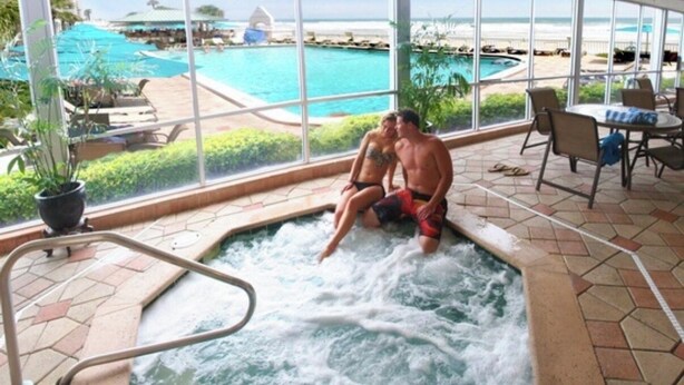 An indoor hot tub with a view of a pool and beach.