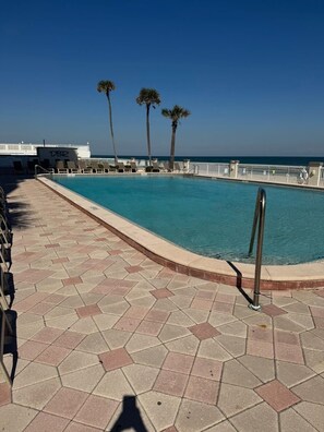 A pool area with a tiled deck, lounge chairs, and palm trees. - Josh’s Daytona Beach Resort 1BR Oceanfront Condo 🏖 (Daytona Beach)