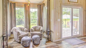 Une pièce chaleureuse avec deux fauteuils et des repose-pieds, une petite table et une grande porte-fenêtre coulissante donnant sur un espace extérieur.