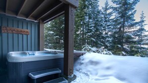 Ein Whirlpool vor einer Holzhütte, mit Stufen, die hinaufführen, umgeben von schneebedeckten Bäumen.