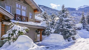 Eine Blockhütte mit einem Balkon, umgeben von schneebedeckten Bäumen und Bergen.