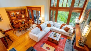 Ein geräumiges Wohnzimmer mit einer großen Eckcouch, einem Essbereich mit Holzmöbeln und großen Fenstern mit Blick auf Grünflächen.