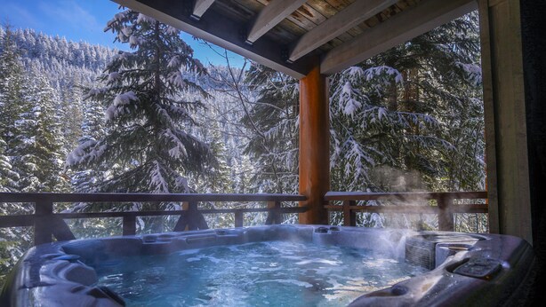 Ein Whirlpool mit Holzterrasse und Blick auf verschneite Bäume.
