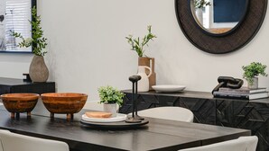 A modern dining area with a dark wooden table, white chairs, and a chandelier.