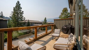 A balcony with wicker furniture, a barbecue grill, and a view of houses and trees.