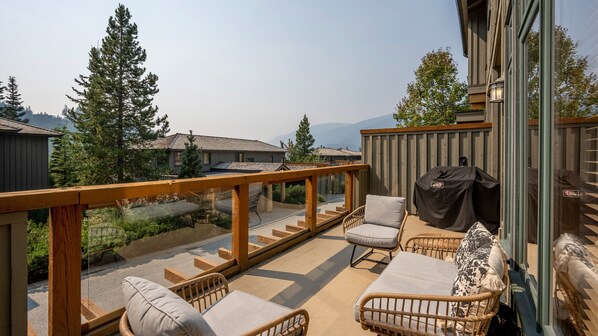 Ein Balkon mit Korbmöbeln, einem Grill und Blick auf Häuser und Bäume.