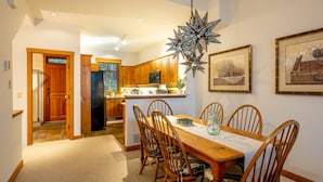 Un comedor con una mesa y sillas de madera, una araña y una cocina al fondo.