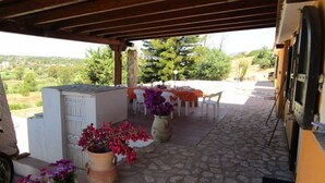 An outdoor patio area with stone flooring, a covered seating area with tables and chairs, and potted plants. - Villa Ingeborg King Room (QUARTU SANT'ELENA)