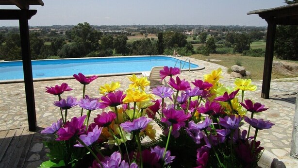 A pool with a clear view of the surrounding landscape, a gazebo structure, and a variety of colorful flowers in the foreground. - Villa Ingeborg King Room (QUARTU SANT'ELENA)