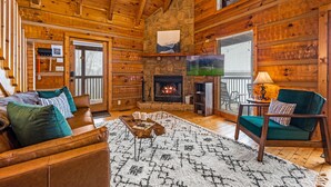 L’intérieur chaleureux d’un chalet avec une cheminée en pierre, des murs en bois, un canapé en cuir et un fauteuil vert.