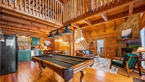 Un intérieur en bois avec une table de billard, des meubles verts et une cheminée.