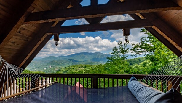 Un hamac sur une terrasse en bois, avec vue sur des montagnes verdoyantes.
