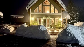 Ein großes, mehrstöckiges Holzhaus mit steiler Dachneigung, beleuchtetem Eingang und einer verschneiten Auffahrt.