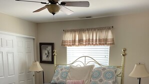 A bedroom with a bed, a ceiling fan, a window with curtains, and two bedside lamps.