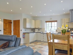 A modern kitchen with white cabinets, a dining area with a wooden table and chairs, and a blue leather sofa. - 3 bedroom accommodation in Tregaron (Tregaron)