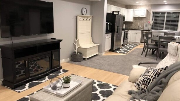 A modern living room with a flat-screen TV, a fireplace, a sofa, and a dining area with a kitchen in the background. - Family Favorite with Indoor Basketball Court (Sandy)