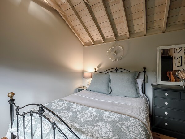Ein Schlafzimmer mit Bett, Nachttisch, Kommode, Spiegel und Wanduhr.