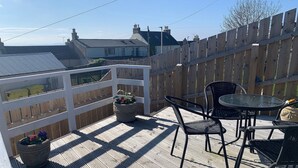 A wooden deck with a white railing, outdoor furniture, and potted plants. - A beautiful coastal cottage in characterful Portmahomack. (Portmahomack, near Dornoch)