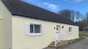 A single-story building with a sloped roof, a small porch with steps, and a door with a window above it. - A beautiful coastal cottage in characterful Portmahomack. (Portmahomack, near Dornoch)